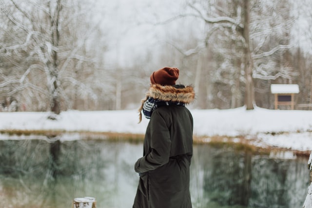 Person standing in front of a pond surrounded by snow