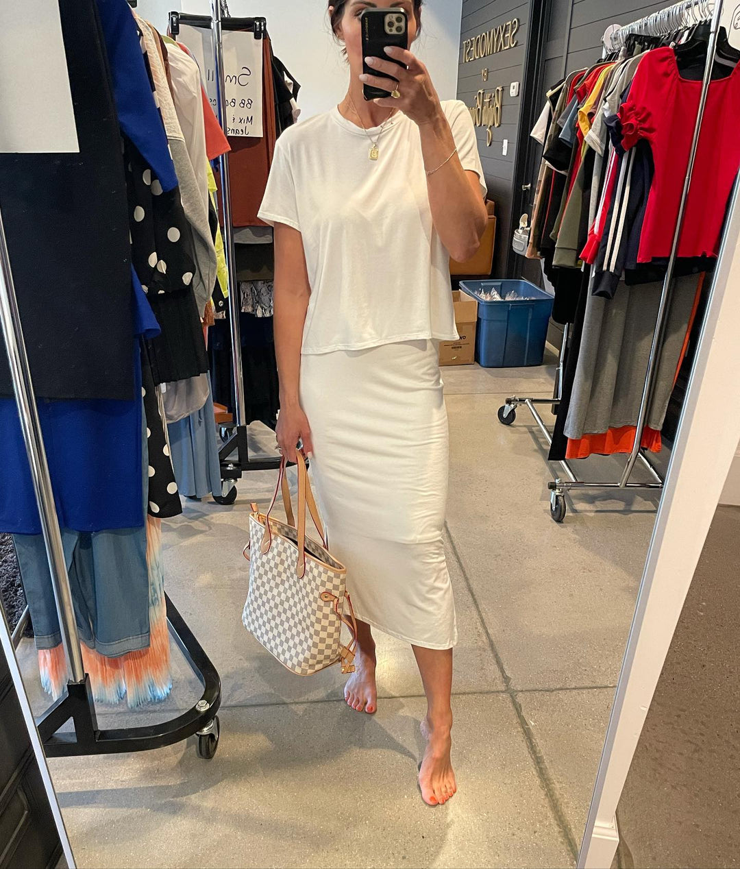 Brigitte taking a mirror selfie wearing a white outfit in a clothing store.