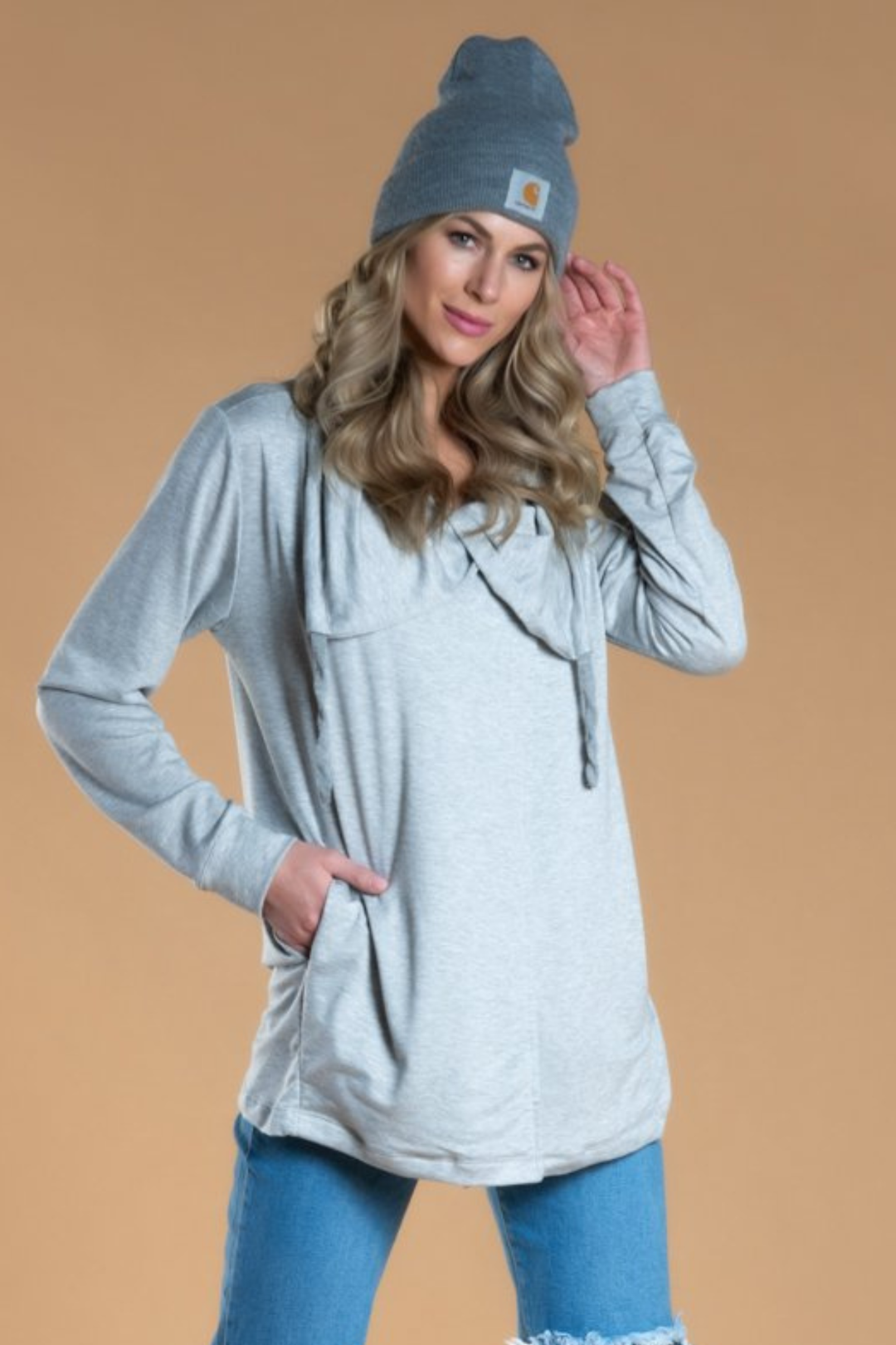 Woman wearing a gray hoodie and blue beanie on a beige background