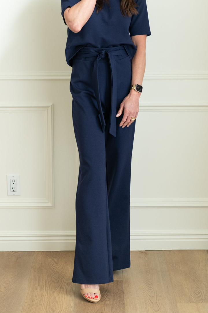 Person wearing a navy blue outfit with wide-leg pants and a matching top against a neutral wall.