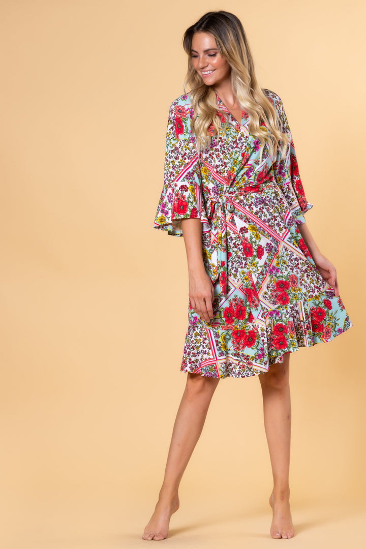A woman standing in a studio setting, wearing a floral print, knee-length, silky robe with ruffle sleeves.